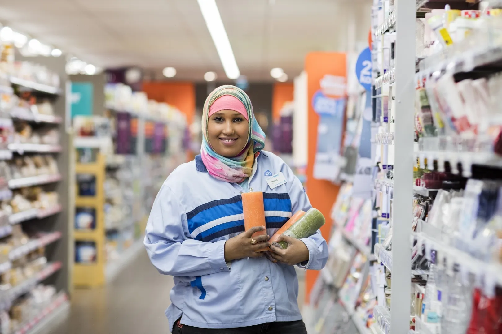 Halima staat in een gangpad bij de Albert Heijn met een aantal producten in haar hand, ze kijkt richting de camera.