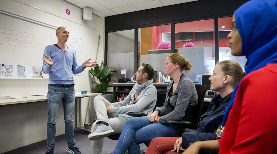 Een trainer staat voor een groep jongeren die in een halve kring zitten