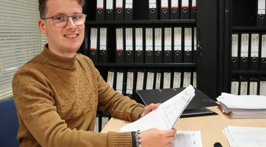 Jonge man zit achter een buro en heeft papieren in zijn handen