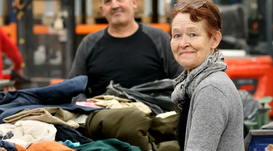 Man en een vrouw in het textielsorteercentrum met in de achtergrond karren met textiel