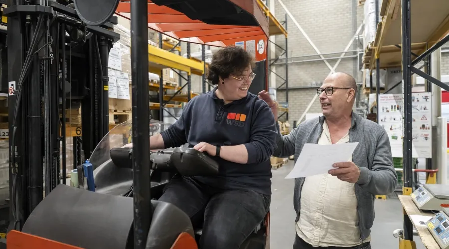 Een jongen op een heftruck krijgt uitleg van zijn werkbegeleider