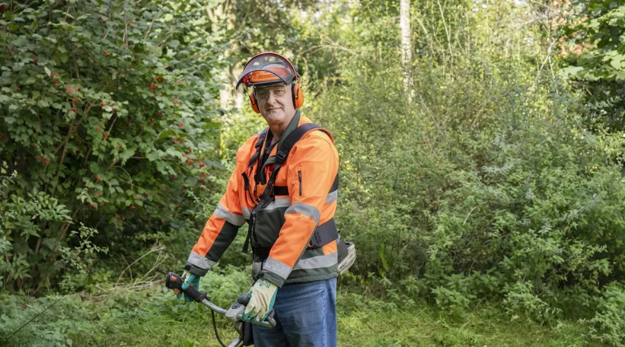 Man werkt in het groen met bosmaaier en kijkt in de camera